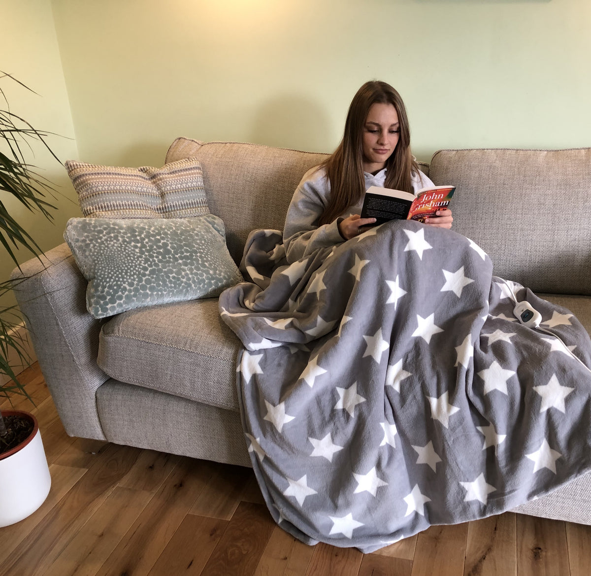 A girl on sofa with heated throw reading a book.